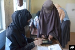 FILE - A woman voter, right, has her finger scanned before casting her vote during parliamentary elections in Kandahar, south of Afghanistan, Oct. 27, 2018.