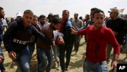 Palestinian protesters help a wounded youth during clashes with Israeli troops along the Gaza Strip border with Israel, east of Khan Younis, Gaza Strip, Friday, March 30, 2018. (AP Photo/Adel Hana)