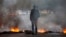 An anti-government protester stands at a burning barricade erected by protesters to block the road to Valle de los Angeles, on the outskirts of Tegucigalpa, Honduras, Dec. 7, 2017. 
