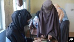 FILE - A woman has her finger scanned before casting her vote during parliamentary elections in Kandahar, Afghanistan, Oct. 27, 2018.