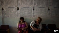 Dua orang perempuan duduk dekat poster pemilu di tempat pemungutan suara di Krasnoarmiisk, provinsi Donetsk, Ukraina timur (24/5).