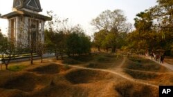 In this file photo, visitors walk by the mass grave of the victims of the Khmer Rouge regime next to a memorial stupa filled with victims' skulls at the Choeung Ek killing field in Phnom Penh, Cambodia. 