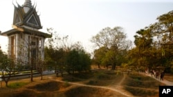 In this file photo, visitors walk by the mass grave of the victims of the Khmer Rouge regime next to a memorial stupa filled with victims' skulls at the Choeung Ek killing field in Phnom Penh. 