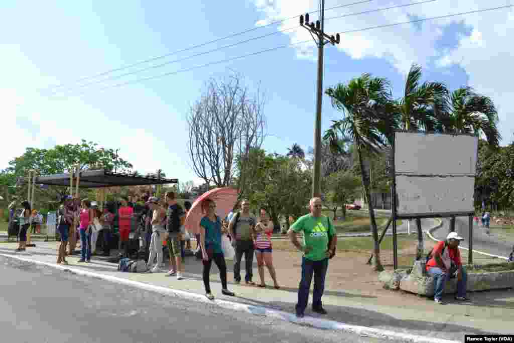 People line up on the sidewalk while waiting for a bus, on the outskirts of Havana. 