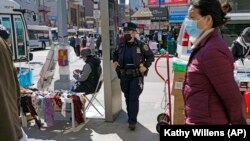 New York Police Department Officer Joanna Derkacz keeps an eye on pedestrians passing her on a busy stretch of Main Street in Flushing, Tuesday, March 30, 2021, in the Queens borough of New York. (AP Photo/Kathy Willens)