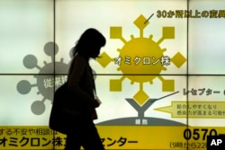 A woman wearing a face mask walks in front of a public awareness notice on the Omicron coronavirus variant, in Tokyo, Jan. 24, 2022.