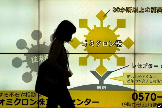 A woman wearing a face mask walks in front of a public awareness notice on the Omicron coronavirus variant, in Tokyo, Jan. 24, 2022.