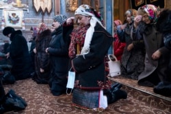 Dr. Viktoria Mahnych, wearing a Hutsul's traditional colorful clothes, crosses herself holding a face mask in her hand because other worshippers forced her to take off her mask. (AP Evgeniy Maloletka)