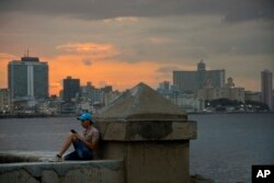 A man chats using his cellphone while sitting on a seawall in Havana, Cuba, Feb. 20, 2019.
