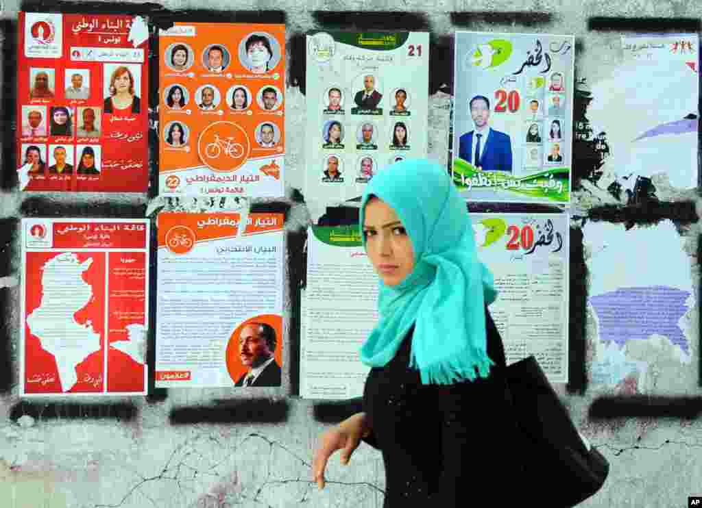 A woman walks past electoral campaign posters for the upcoming parliamentary elections in Tunis, Tunisia. 