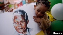 Two-year-old Precious Mali holds a picture of former South African President Nelson Mandela as well-wishers gather outside the Medi-Clinic Heart Hospital where Mandela is being treated in Pretoria June 28, 2013. 