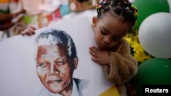 Bé Precious Mali, 2 tuổi, với hình cựu Tổng thống Nam Phi Nelson Mandela giữa những người tập trung trước bệnh viện nơi ông Mandela đang được điều trị ở Pretoria, ngày 28/6/2013. 