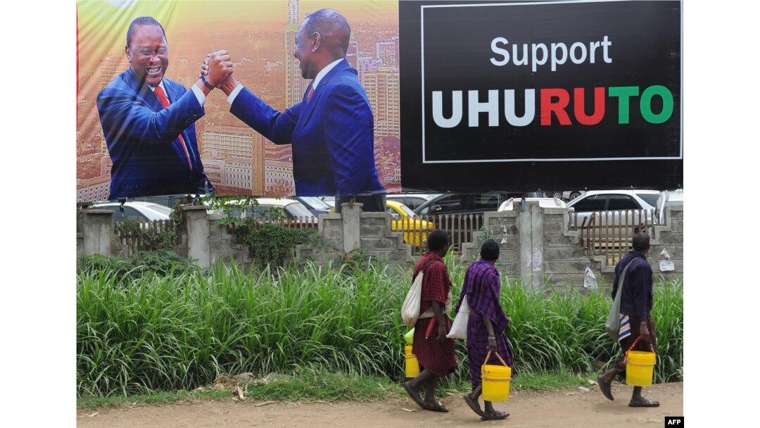 People walk past a campaign poster of Kenya's President Uhuru Kenyatta and Deputy President William Ruto, in Nairobi, Oct. 23, 2017, ahead of the repeat elections.