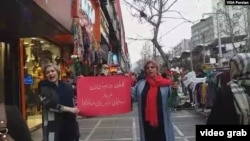 Two unveiled Iranian women mark International Women's Day on Tehran's Valiasr Street, March 8, 2019, holding a red sign that says the occasion brings hope for a just world for all humanity.