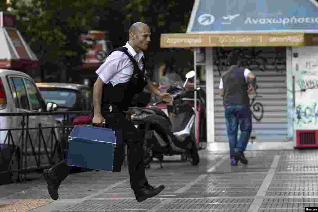 Seorang petugas keamanan membawa yang dari cabang Bank Nasional di Athena, Yunani. Mitra-mitra Eropa Yunani tidak memperpanjang dana talangan kepada Athena, dan menyebabkan negara tersebut terancam dikeluarkan dari mata uang gabungan euro dan mempengaruhi ekonomi Eropa dan luar Eropa.