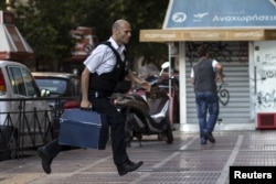 FILE - A security worker brings money to a National Bank branch in Athens, Greece, June 28, 2015.