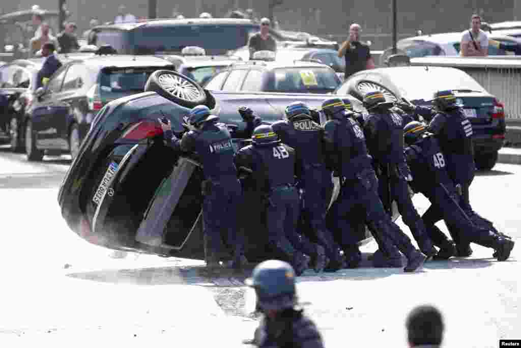 French riot police push an overturned car as striking taxi drivers demonstrate at the Porte Maillot to block the traffic on the ring road during a national protest against car-sharing service Uber, in Paris.