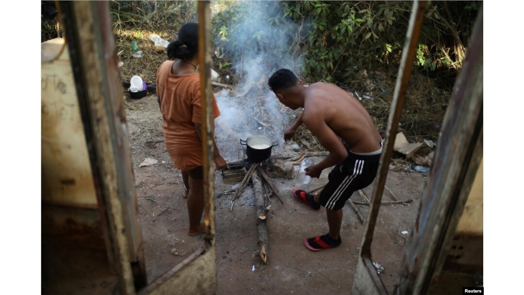 Venezuelans Hildemaro Ortiz and Ixora Sanguino cook outside of an abandoned bus in the border city of Pacaraima, Brazil, April 13, 2019.