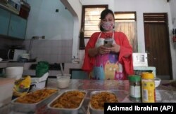 Rani Nurwitawati checks her mobile phone as she prepares food for her online customers at her residence in Bekasi on the outskirts of Jakarta, Indonesia, Nov. 26, 2020.