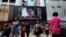 People cross a street in front of a monitor showing file footage of Edward Snowden, a former contractor for the U.S. National Security Agency (NSA), with a news tag (L) saying he has left Hong Kong, outside a shopping mall in Hong Kong, June 23, 2013.