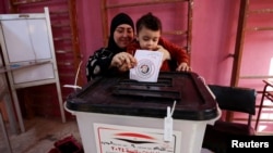 FILE - A woman casts a ballot with a child, at a polling station on the second day of the presidential election in Giza, Egypt, December 11, 2023. 