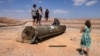 People stand on top of the remains of an Iranian missile in the Negev desert near Arad, on October 2, 2024, in the aftermath of an Iranian missile attack on Israel.