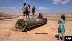 People stand on top of the remains of an Iranian missile in the Negev desert near Arad, on October 2, 2024, in the aftermath of an Iranian missile attack on Israel.