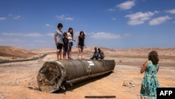 Orang-orang berdiri di atas sisa-sisa rudal Iran di gurun Negev dekat Arad, 2 Oktober 2024, setelah serangan rudal Iran terhadap Israel. (Menahem KAHANA / AFP)