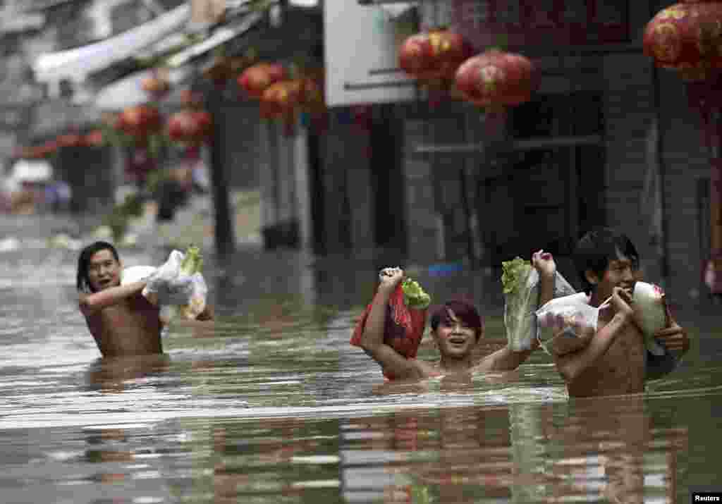 Para warga mengangkat kantong-kantong hasil berbelanja sambil mengarungi jalan yang banjir akibat Topan Fitow yang melanda kota Wenling, provinsi Zhejiang (8/10).