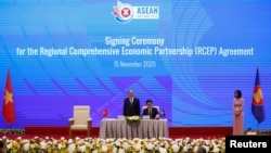 Vietnam's Industry and Trade Minister Tran Tuan Anh (C) signs as Vietnam's PM Nguyen Xuan Phuc (L) witnesses during the signing ceremony of the Regional Comprehensive Economic Partnership Agreement during the 37th ASEAN Summit in Hanoi, Nov. 15, 2020.