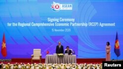 Vietnam's Industry and Trade Minister Tran Tuan Anh (C) signs as Vietnam's PM Nguyen Xuan Phuc (L) witnesses during the signing ceremony of the Regional Comprehensive Economic Partnership Agreement during the 37th ASEAN Summit in Hanoi, Nov. 15, 2020.