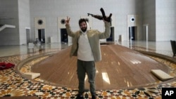 A man holds an AK-47 and flashes the victory sign as he poses for a photo in a hall of Syrian President Bashar Assad's presidential palace in Damascus, Dec. 8, 2024.