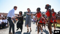 FILE - Prince Harry, Duke of Sussex and Meghan, Duchess of Sussex, dance during a visit to the "Justice desk", an NGO in the township of Nyanga in Cape Town, as they begin their tour of the region, Sept. 23, 2019..