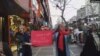 Two unveiled Iranian women mark International Women's Day on Tehran's Valiasr Street, March 8, 2019, holding a red sign that says the occasion brings hope for a just world for all humanity.