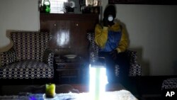 FILE - A Kenyan sips a cup of tea as she sits in her sitting room with emergency light as there was no electricity Saturday, Aug. 26 2023. 