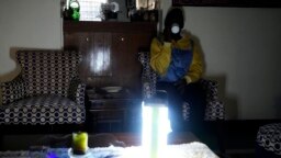 Seorang warga Kenya tampak meminum segelas teh di rumahnya yang diterangi lampu darurat saaat pemadaman melanda Kenya pada 26 Agustus 2023. (Foto: AP/Abdul Azim Sayyid)