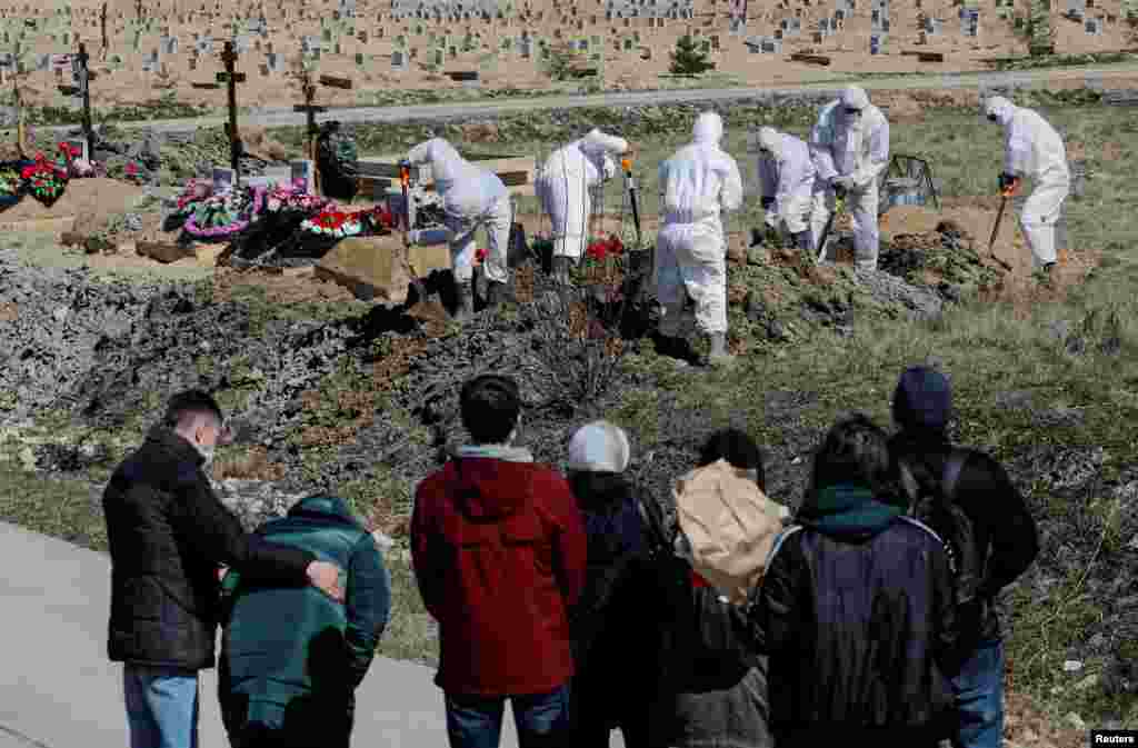 Mourners gather as grave diggers wearing personal protective equipment (PPE), bury a coronavirus disease (COVID-19) victim in the special purpose section of a graveyard on the outskirts of St. Petersburg, Russia.