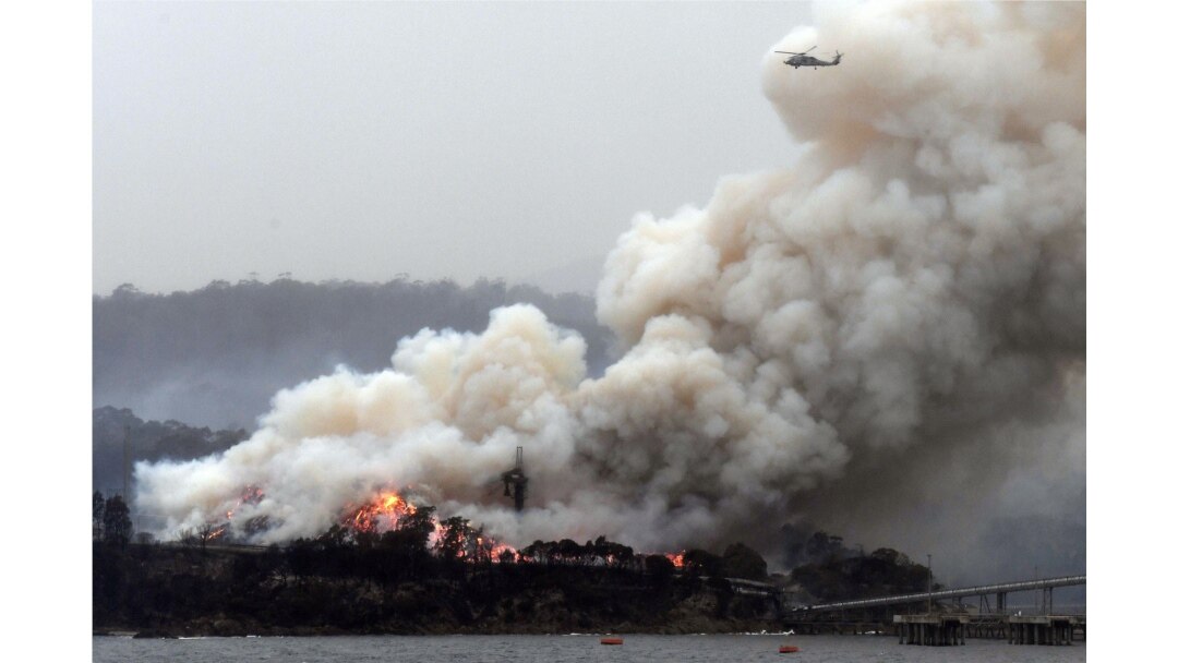 A military helicopter flies above a burning woodchip mill in Eden, New South Wales, Australia, Jan. 6, 2020.