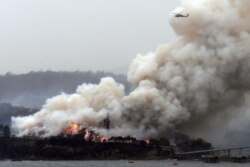 A military helicopter flies above a burning woodchip mill in Eden, New South Wales, Australia, Jan. 6, 2020.