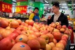 A woman wearing a uniform with the logo of an American produce company helps a customer shop for apples a supermarket in Beijing, China, March 23, 2018.