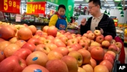 A woman wearing a uniform with the logo of an American produce company helps a customer shop for apples a supermarket in Beijing, China, March 23, 2018.