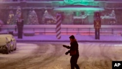 A pedestrian walks across an intersection as snow falls in downtown Indianapolis, Dec. 15, 2019. 