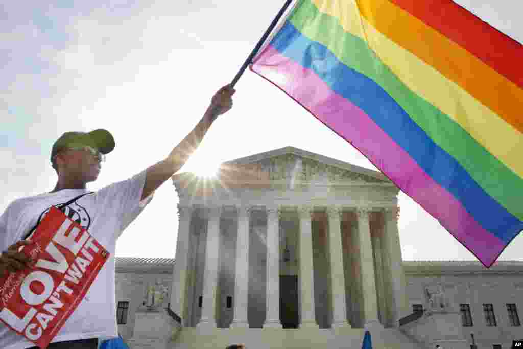 Carlos McKnight melambaikan bendera pelangi sebagai tanda dukungan terhadap pernikahan sesama jenis di luar Mahkamah Agung AS, di Washington, D.C. Mahkamah ini pada hari Jumat menyatakan pasangan sesama jenis memiliki hak untuk menikah di 50 negara bagian AS.