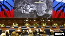 Russian military officials sit under screens with satellite images purportedly showing evidence of Turkey's oil trade with the Islamic State group, during a briefing in Moscow, Russia, Dec. 2, 2015.