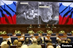 Defense Ministry officials sit under screens with satellite images on display during a briefing in Moscow, Dec. 2, 2015.