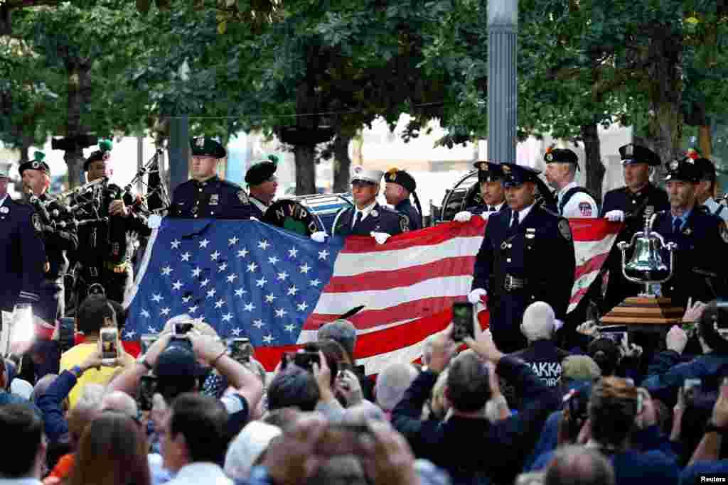 Anggota Kepolisian dan Pemadam Kebakaran memegang bendera Amerika yang berkibar di atas World Trade Center di Museum dan Tugu Peringatan Nasional 11 September atau National 911 Memorial and Museum saat upacara peringatan 16 tahun serangan 11 September 2001 di New York, 11 September 2017.