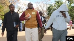 Holding a Bible, Pastor Evan Mawarire, center, walks into the court building while handcuffed to his driver, Ocean Chihota, in Harare, Zimbabwe, June 28, 2017. (S. Mhofu/VOA)