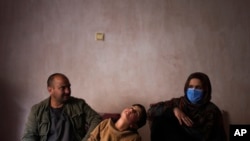Sanam, a bacha posh, a girl living as a boy, sits next to her mother and father during an interview in their house, in Kabul, Afghanistan, Dec. 7, 2021.