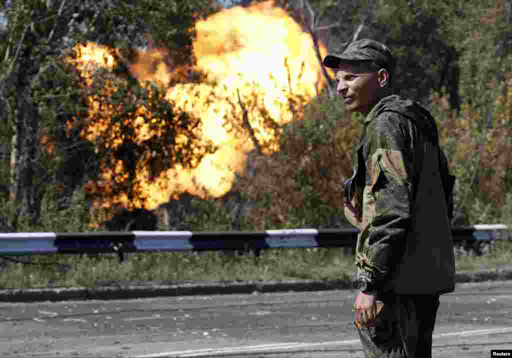 An armed pro-Russian separatist looks on as flames erupt from a gas pipeline after a shelling in Donetsk, Aug. 15, 2014.