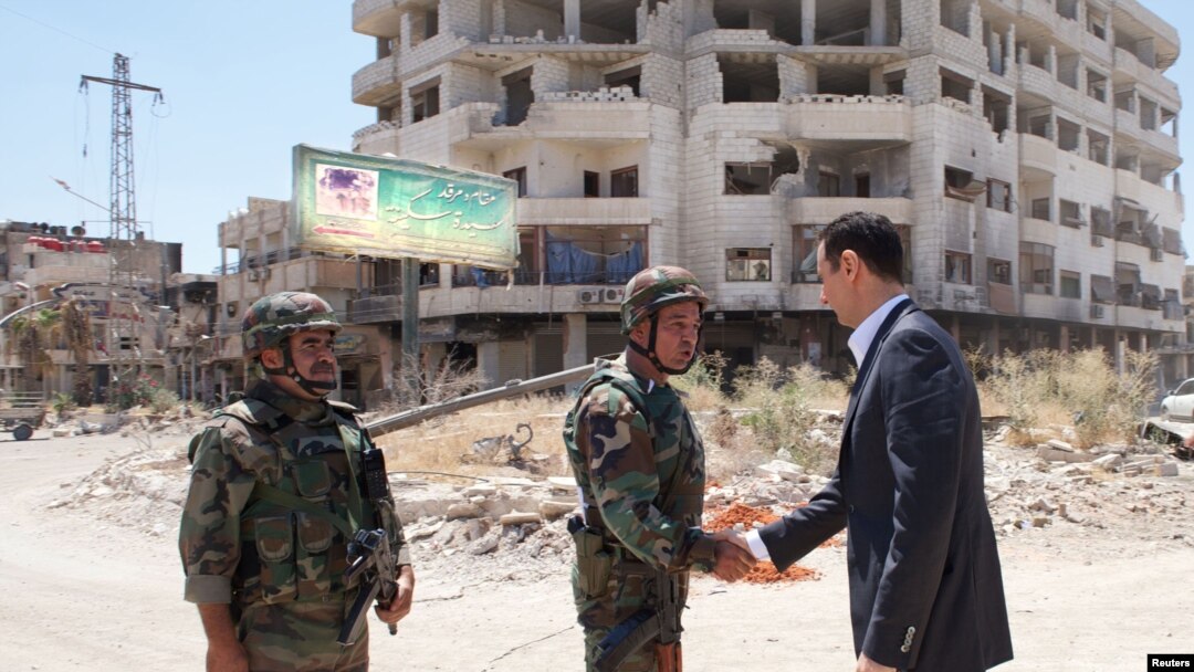 Presiden Suriah Bashar al-Assad berjabat tangan dengan seorang personel militer dalam kunjungannya ke situs militer di Darya awal Agustus.